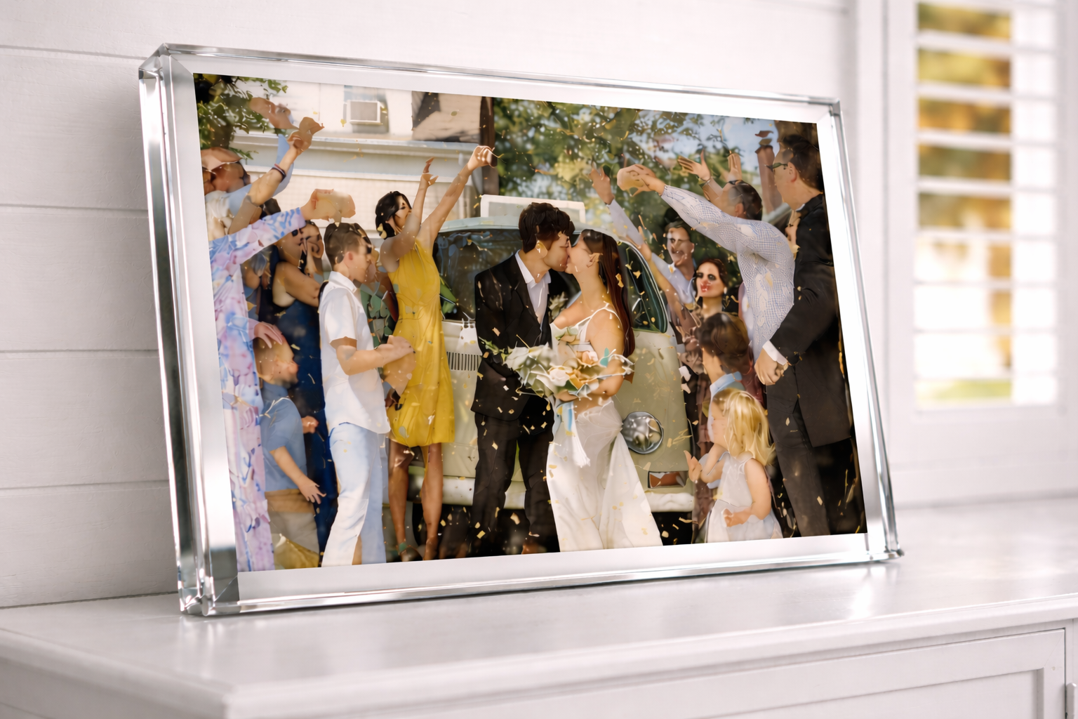 Framed wedding photo of couple kissing while guests throw confetti, with vintage car in background