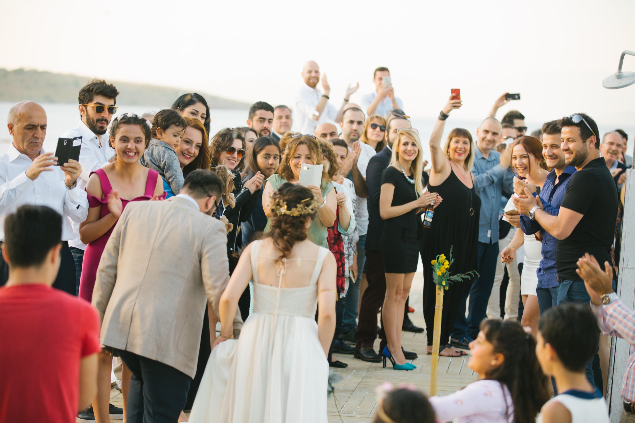 Bride and groom facing wedding guests who are clapping and taking photos at outdoor seaside ceremony