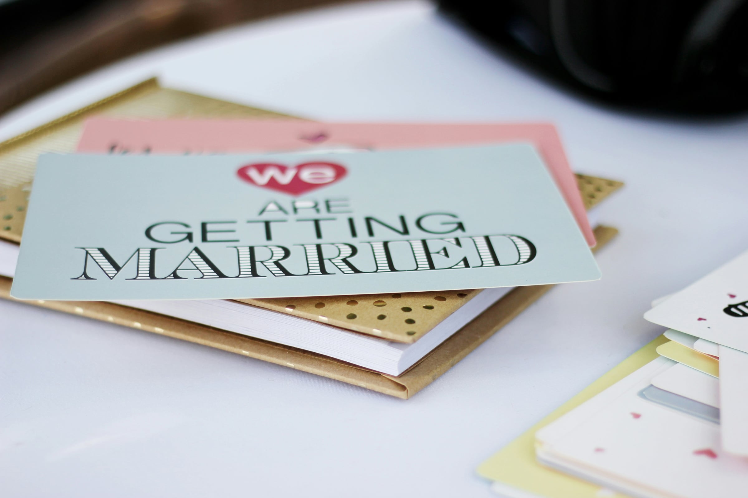 Wedding invitation card with "We are getting married" text and heart icon, stacked on gold notebooks and stationery