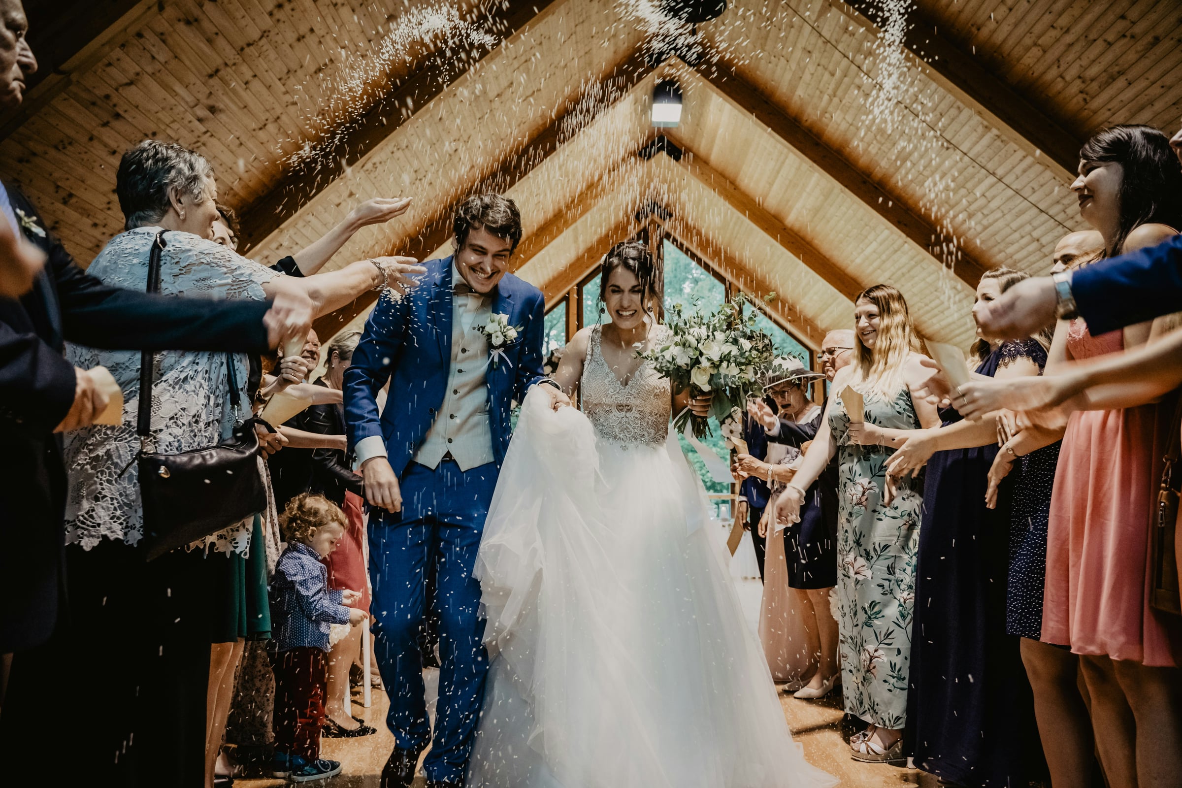 Newlywed couple walking through confetti thrown by guests inside wooden chapel venue